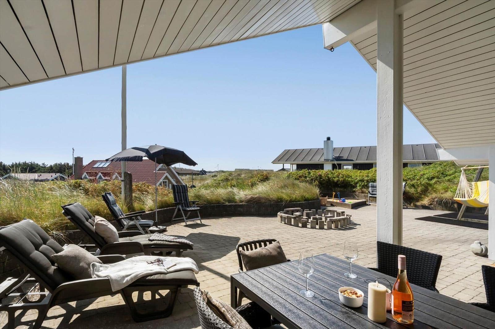 Terrasse mit Liegestühlen, Tisch und Blick auf Grünfläche und Häuser.