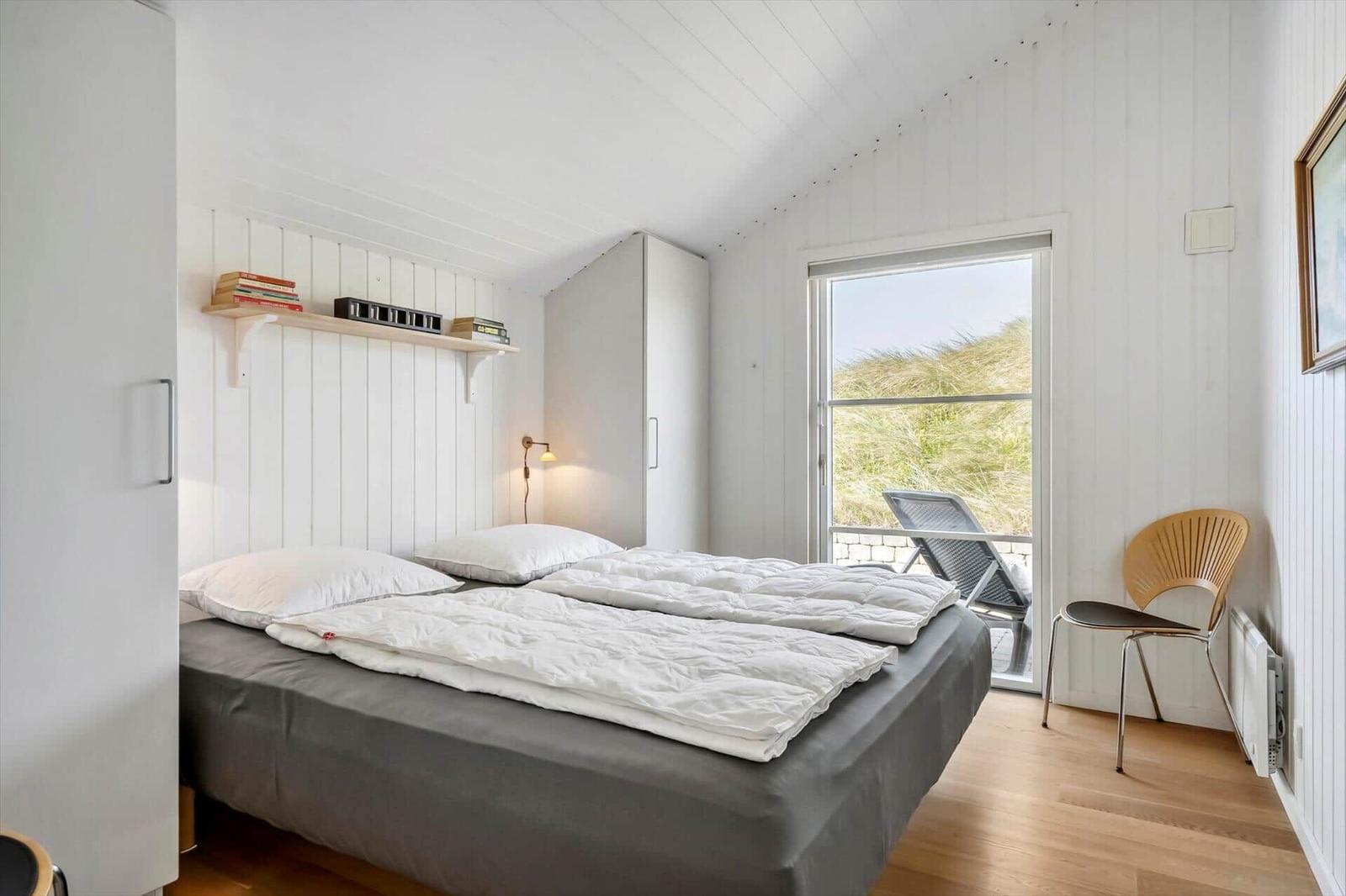 Schlafzimmer mit Bett, Schrank und Fenster zum Balkon mit Sicht auf Gras.