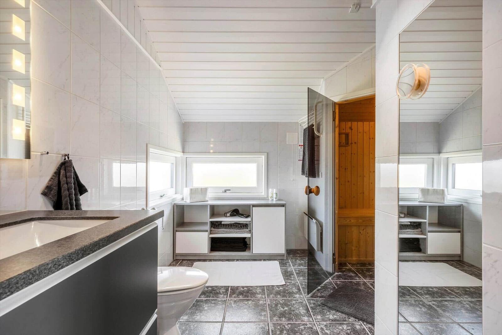 Badezimmer mit Dusche, Toilette und Sauna. Weiße Wände und dunkle Fliesen.