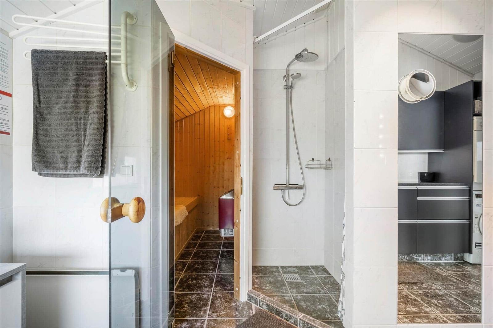 Dusche, Sauna und Küche in einem Raum mit weißen Wänden und dunklem Boden.