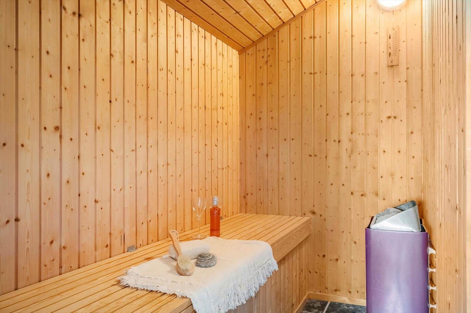 Sauna mit Holzwand, Sitzbank, Flasche, Glas und Handtuch.