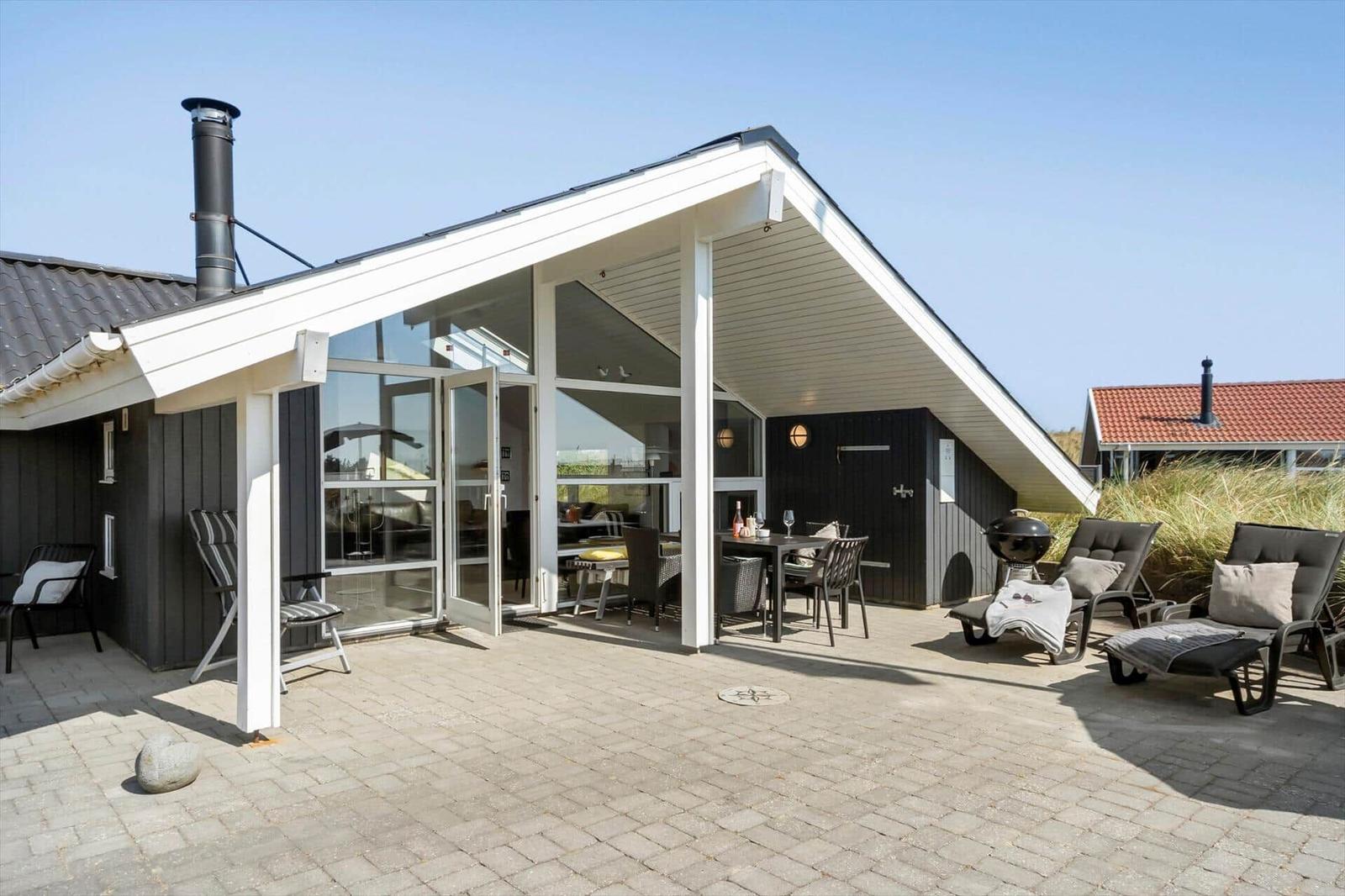 Terrasse mit Grill, Liegestühlen und Blick ins Haus. Glasfront und schwarz-weiße Fassade.