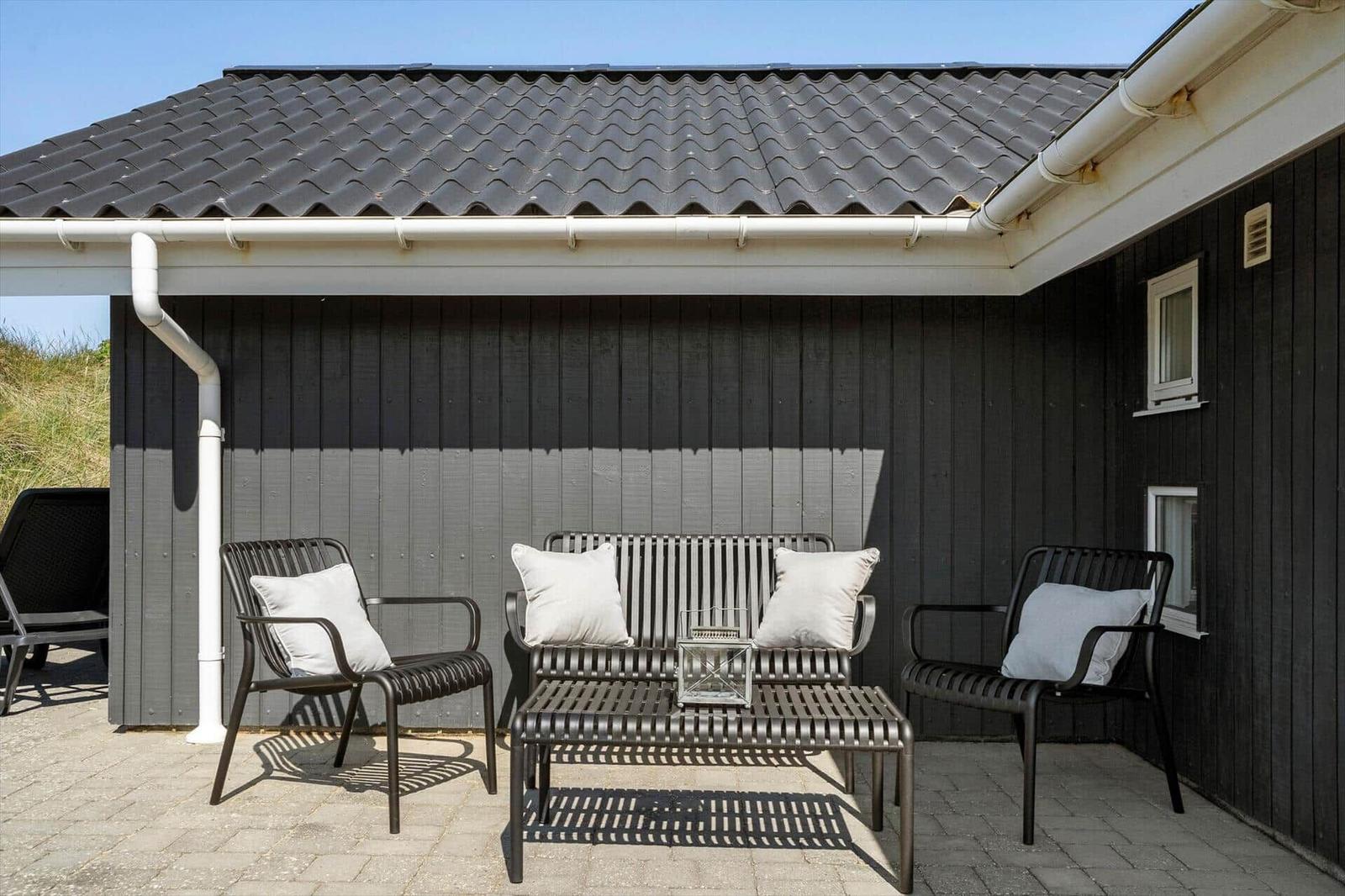 Terrasse mit Sitzgruppe und schwarzem Holzhaus mit Dachrinne.