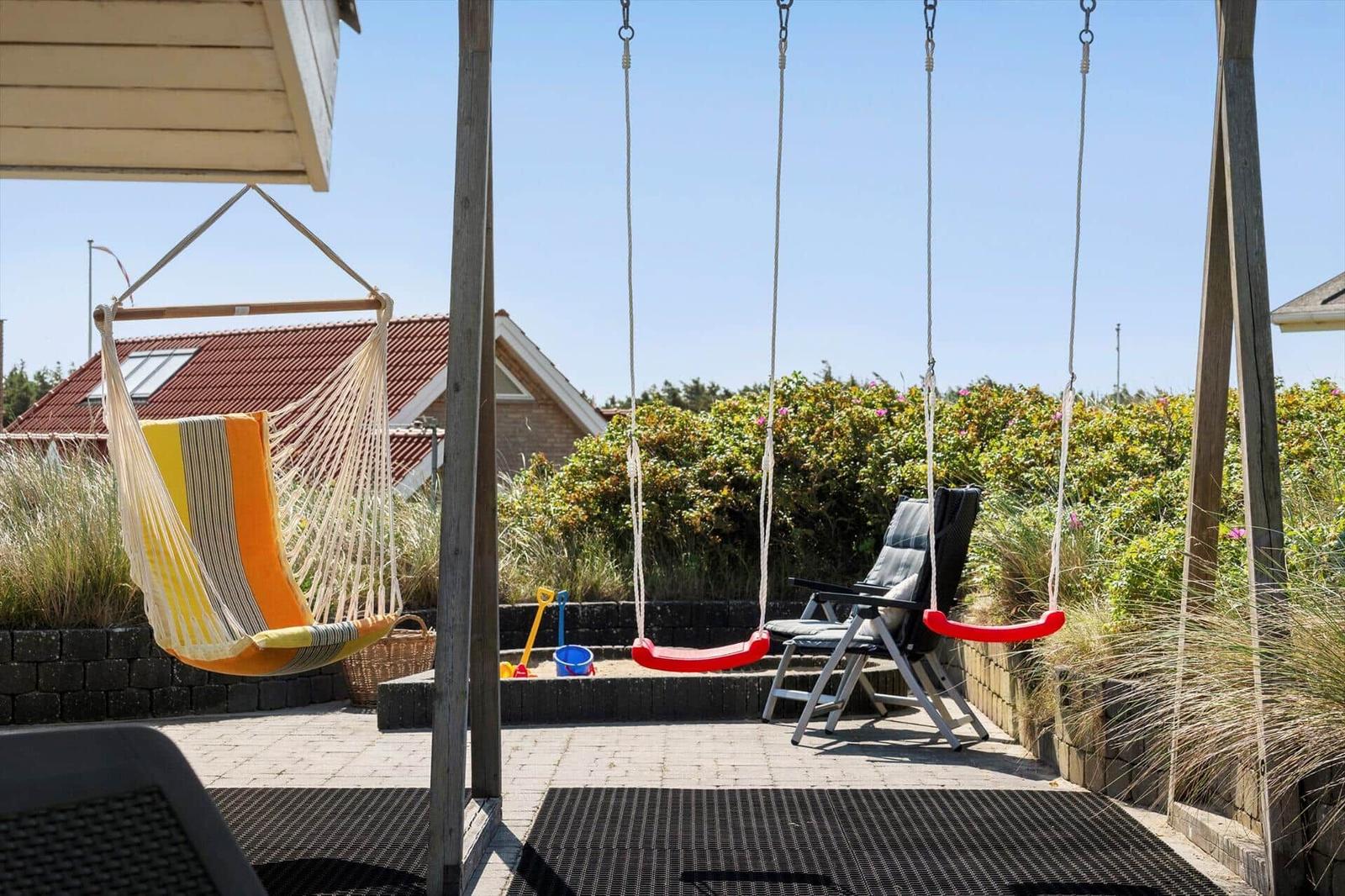 Terrasse mit Hängemattenschaukel und rotem Schaukelstuhl, Spielzeug und Sitzgelegenheiten.