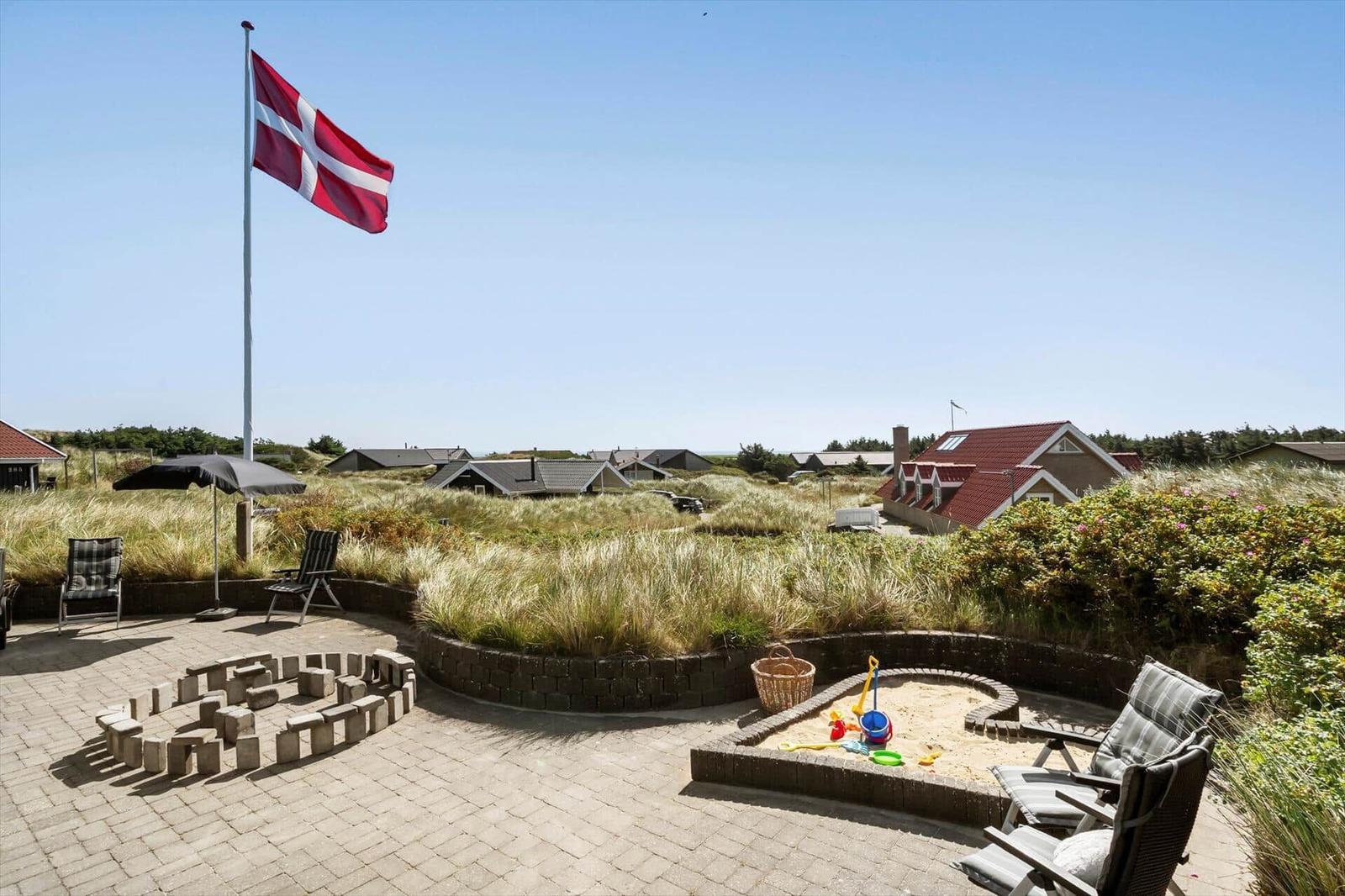 Terrasse mit Sandkasten, Flagge und Gartenmöbeln. Hintergrund: Dänenflagge und Ferienhäuser.
