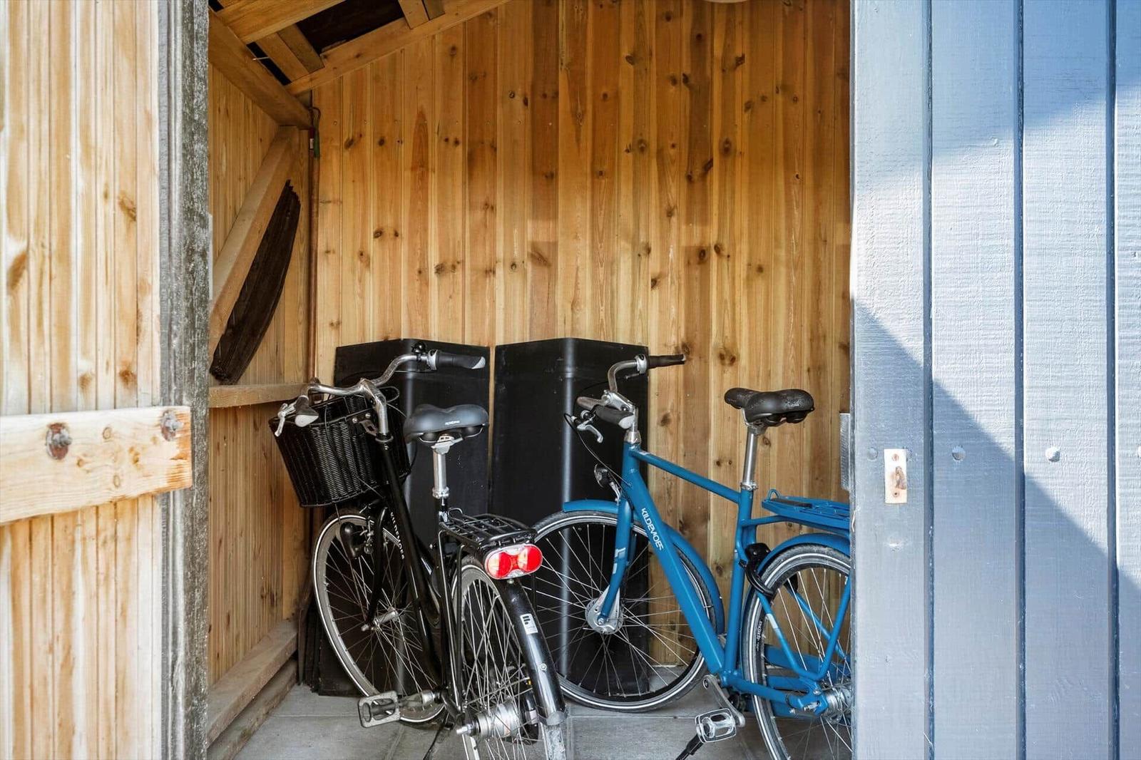 Zwei Fahrräder stehen in einem Holzstall. Ein schwarzes mit Korb, ein blaues.