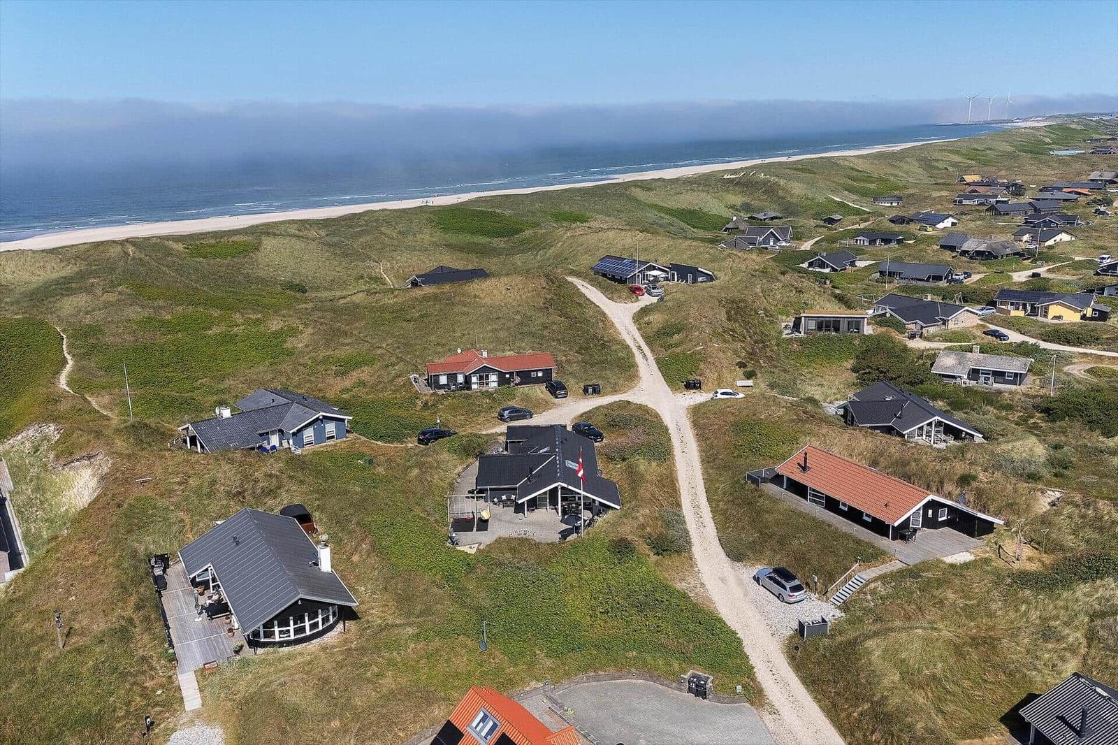 Dorf mit Häusern auf Dünen, Strand und Meer im Hintergrund.