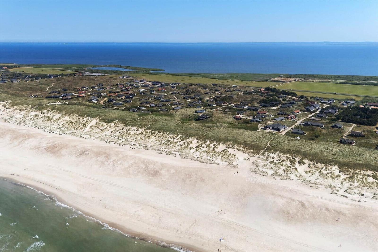 Aerielansicht einer Küstenlandschaft mit Strand, Dünen und Wohnhäusern.