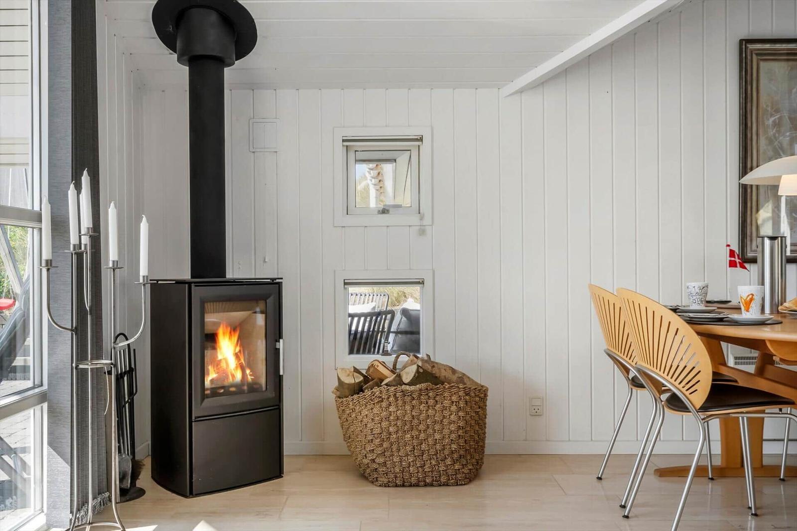 Kaminofen mit Holzstapel, Essbereich und Fenster im Wohnraum.