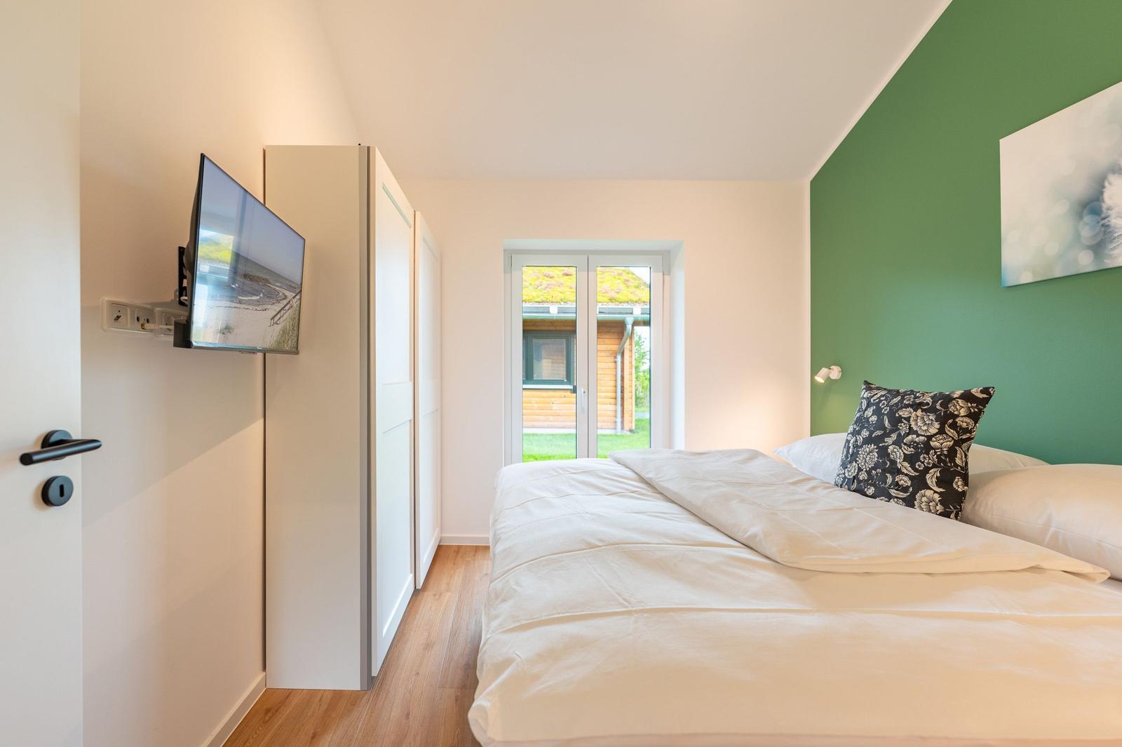 Schlafzimmer mit Bett, Fernseher und Blick auf Garten.