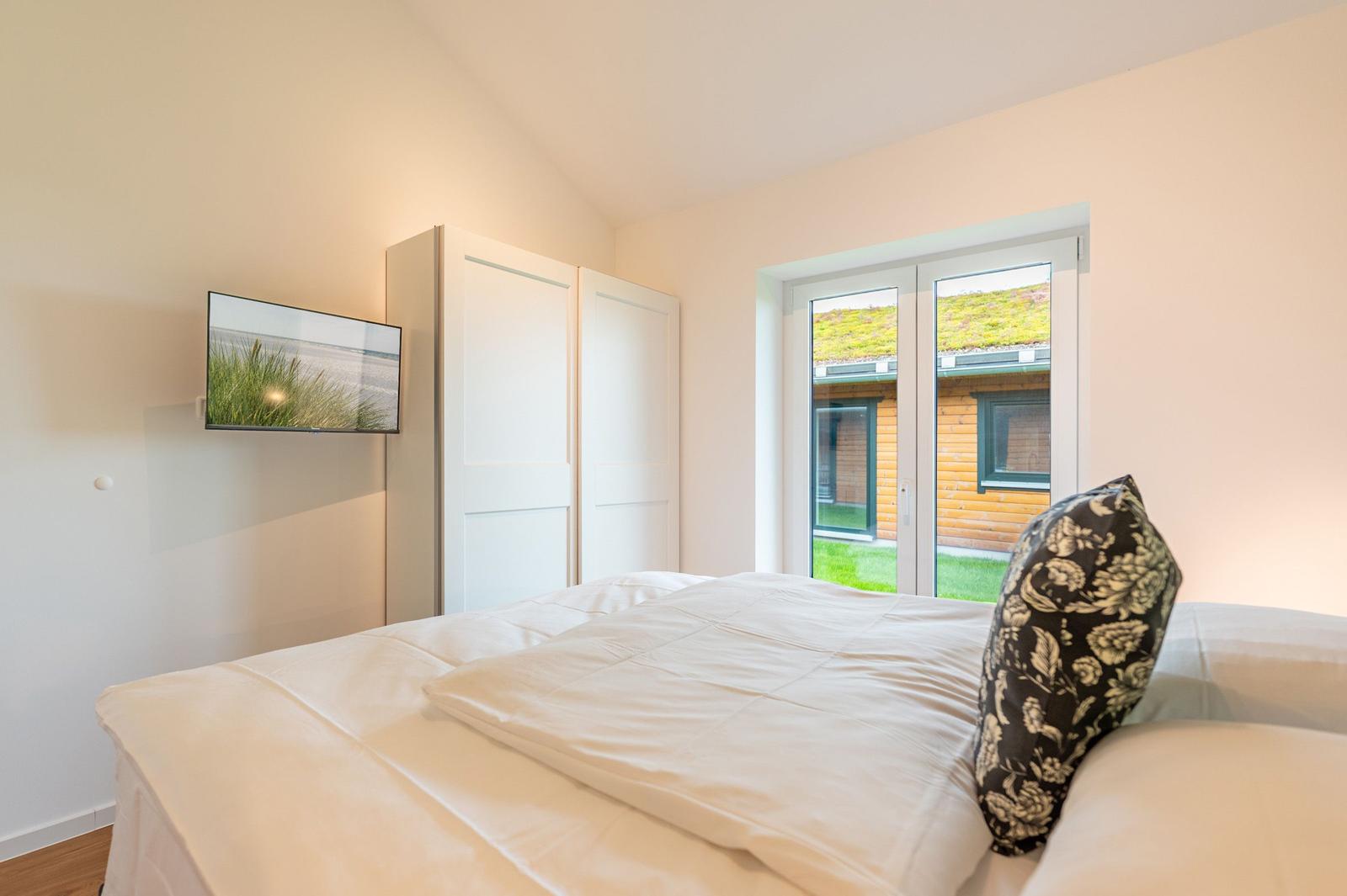 Schlafzimmer mit Bett, TV und Fenster zur Außenterrasse.