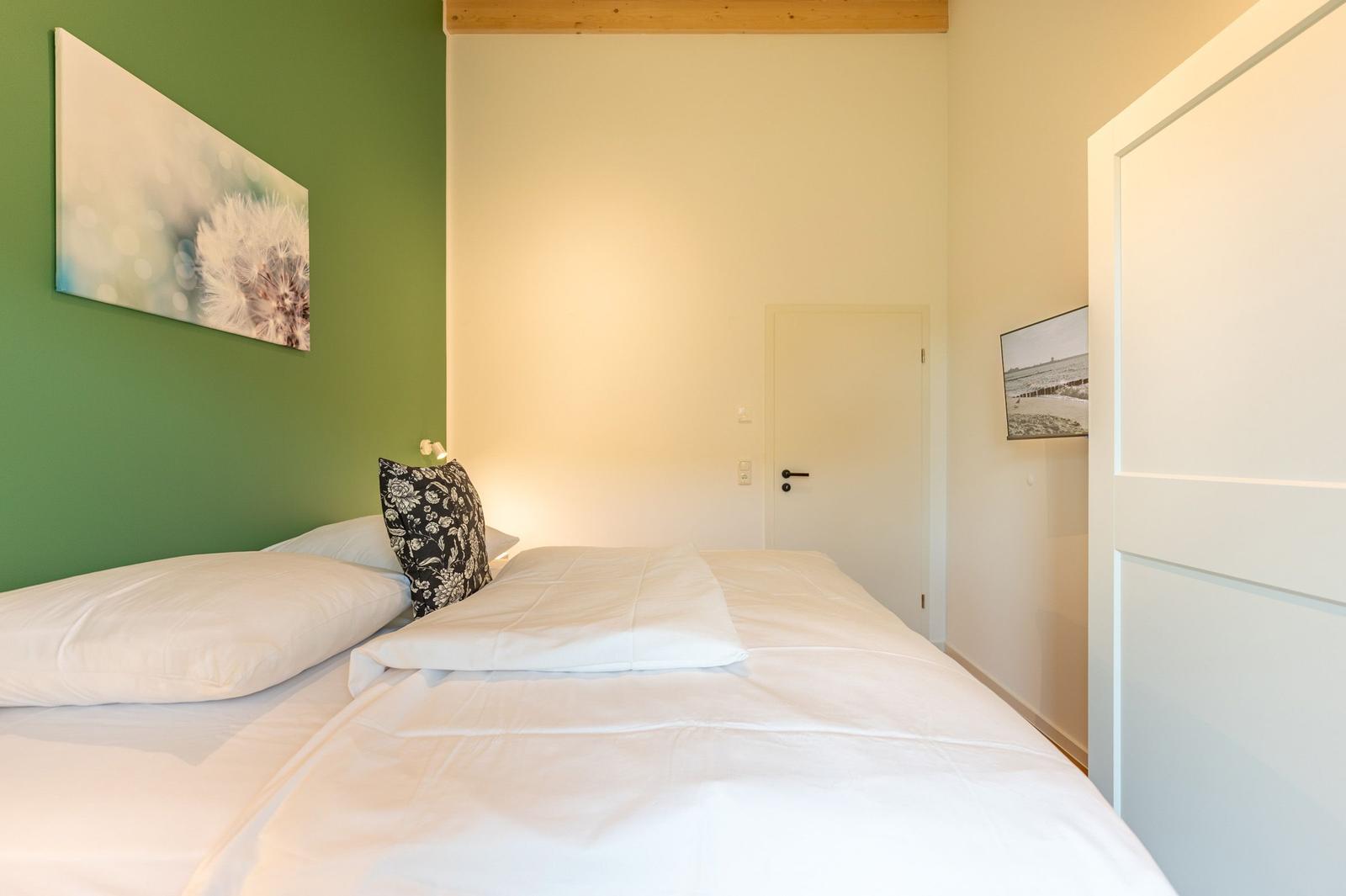 Schlafzimmer mit Bett, grüner Wand und Wandbild