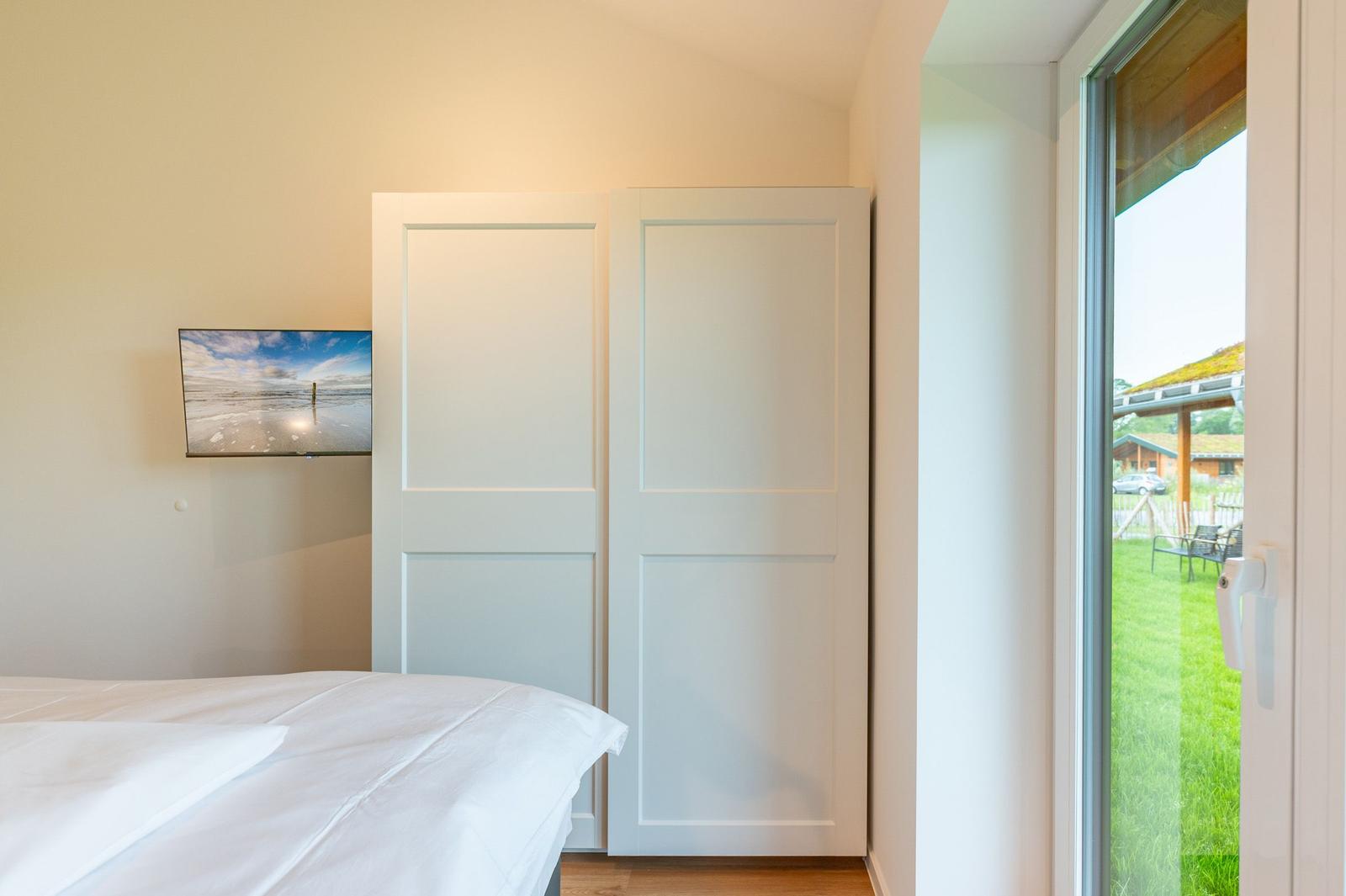 Schlafzimmer mit Bett, TV und Glasfront zum Garten.