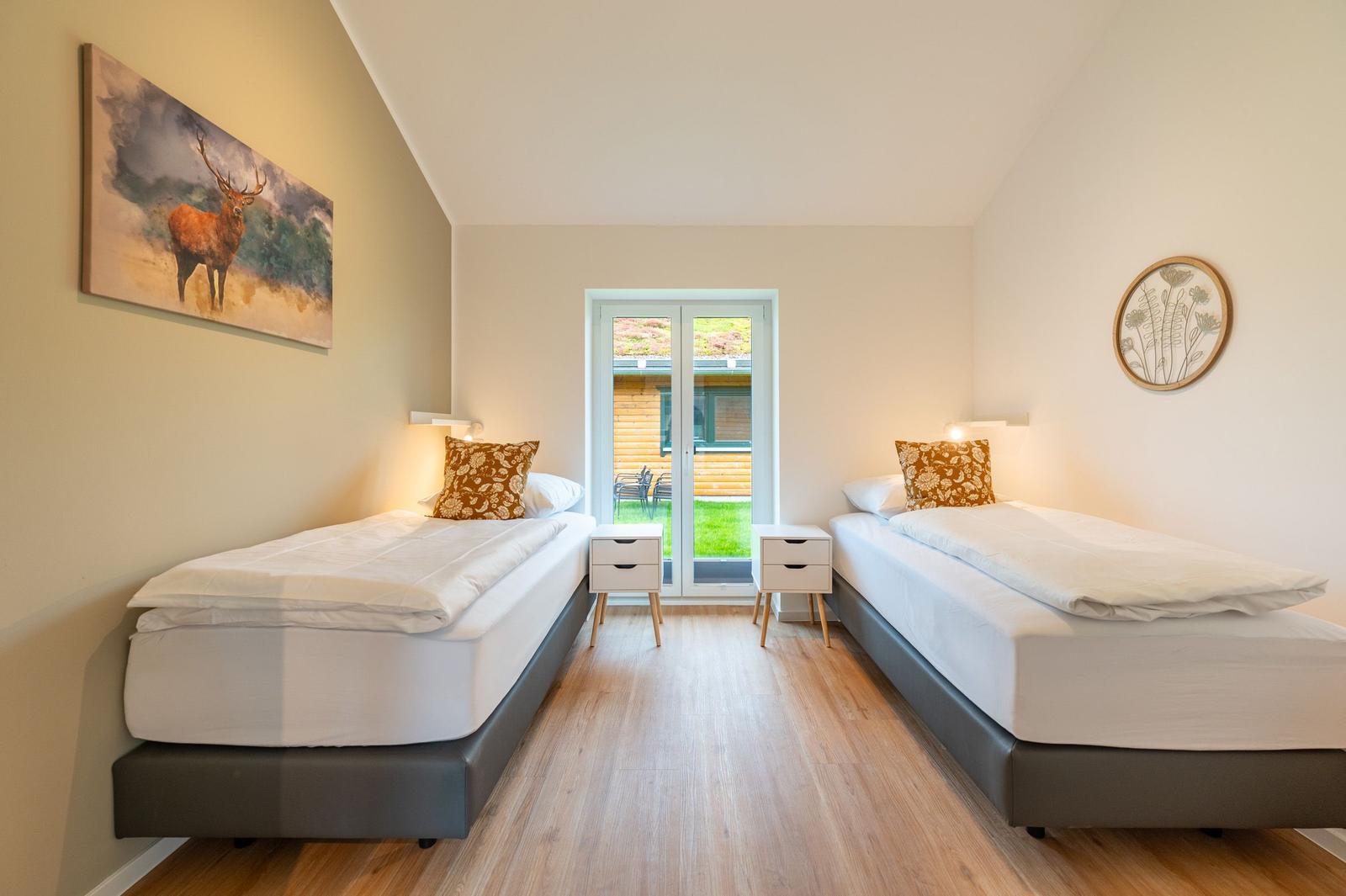 Zwei Betten mit weißen Laken, Holzboden und Fenster zum Garten.