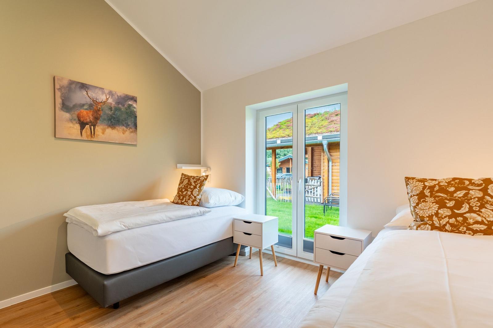 Zwei Betten mit weißen Laken und Holzfußboden. Fenster mit Blick auf Garten.