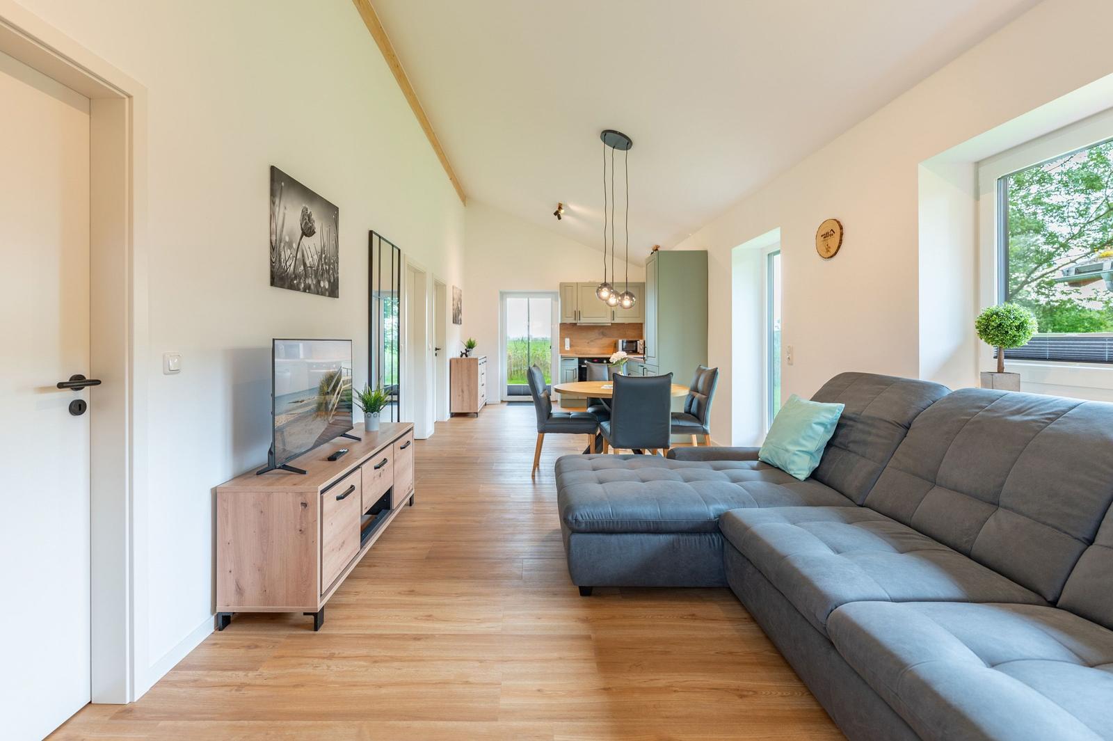 Wohnzimmer mit Sofa, TV und Essbereich im Hintergrund.