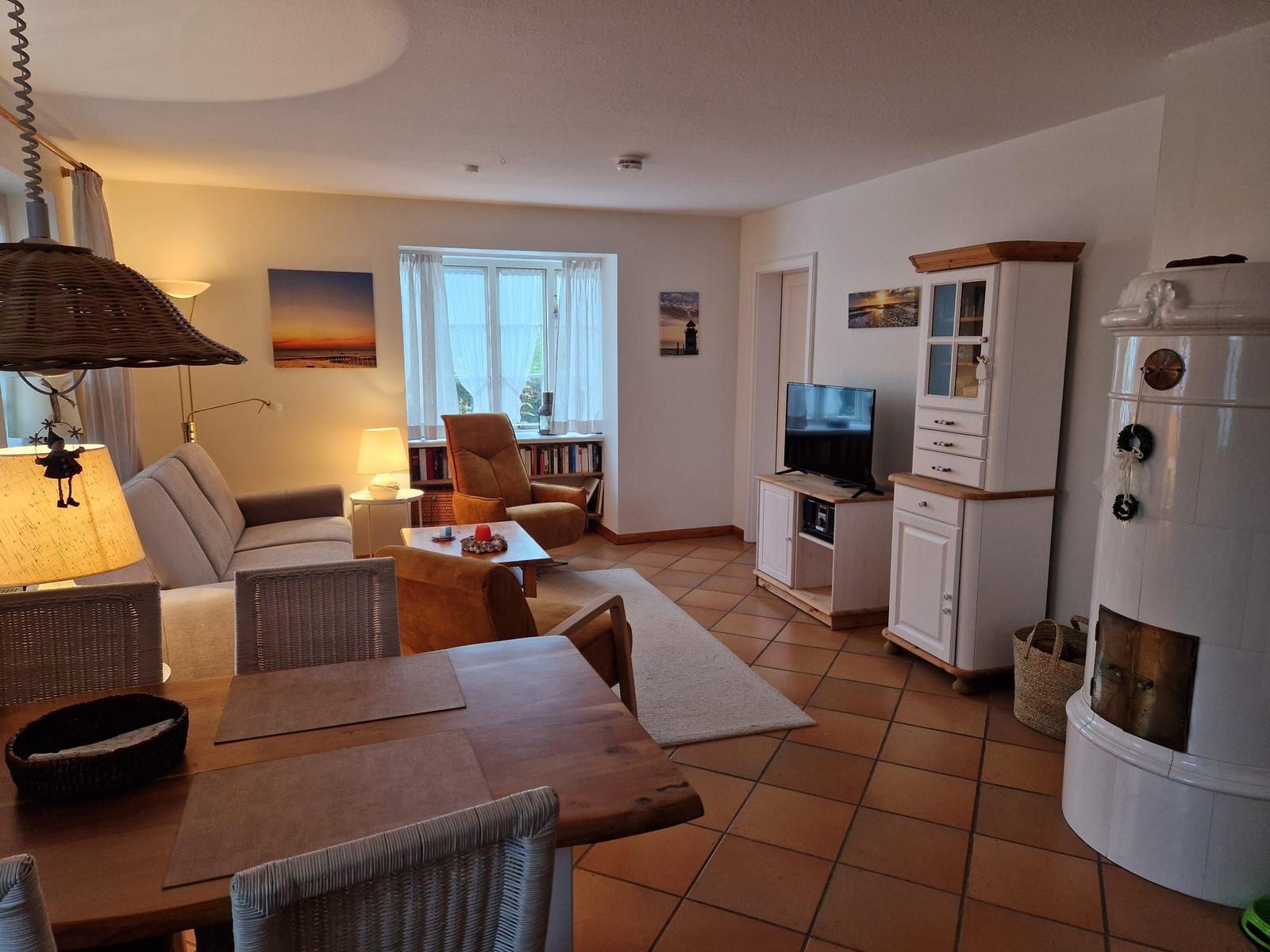 Wohn- und Essbereich mit Sofa, TV und Kaminofen. Holztisch und Stühle.
