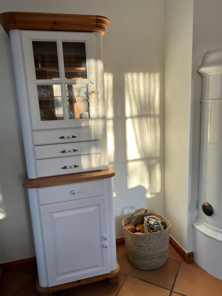 Hochschrank mit Glasfront und Schubladen, daneben Korb mit Holz und Büchern.