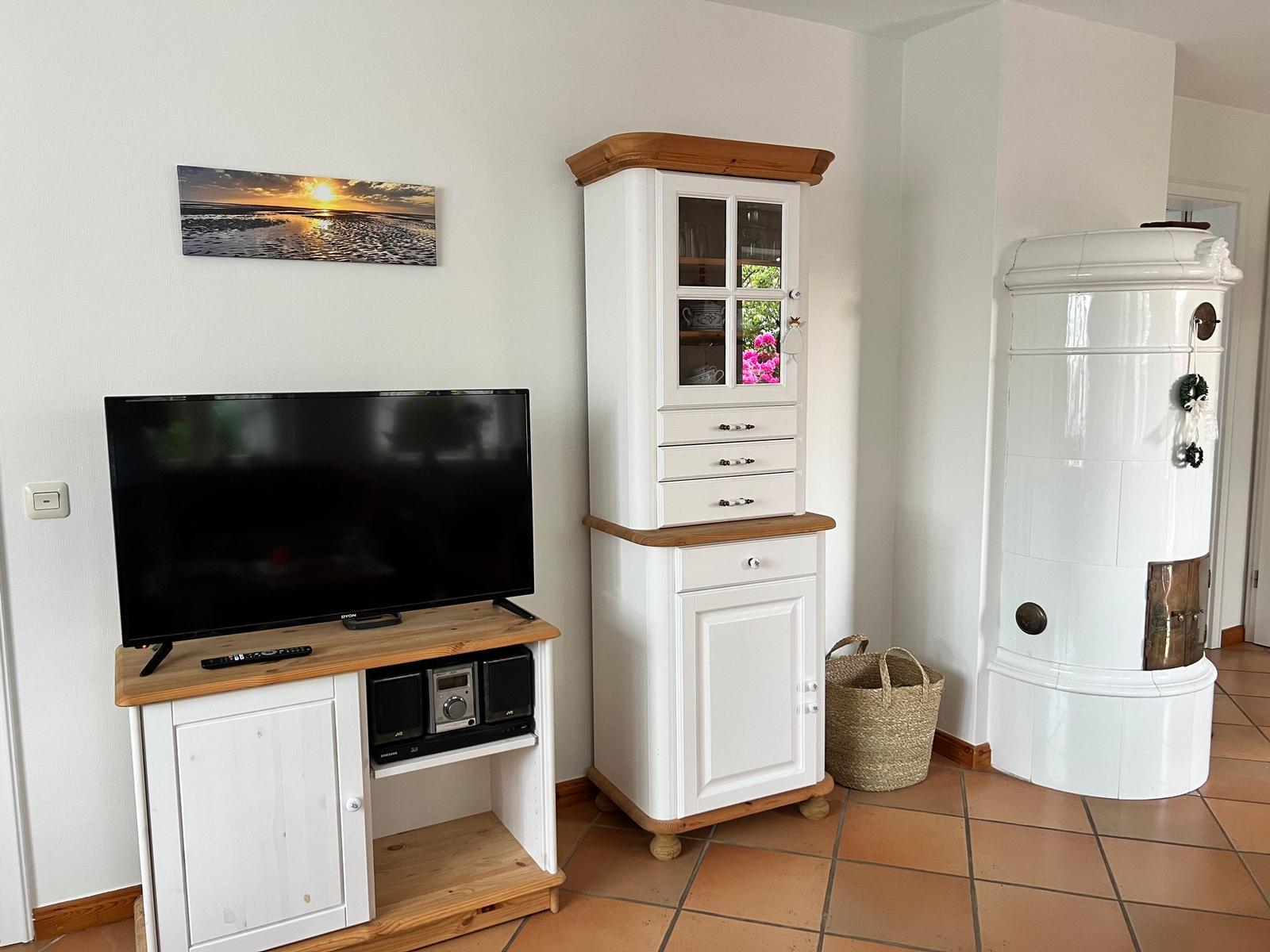 TV auf Holzregal, weißer Schrank und Ofen im Raum.