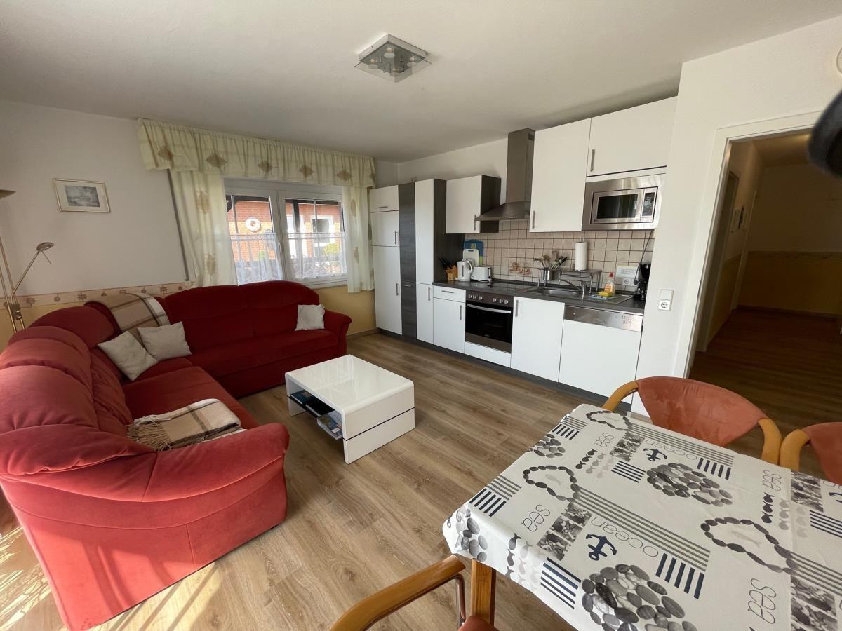 Wohnküche mit rotem Sofa, Küchenschränken und Esstisch mit Tischdecke.