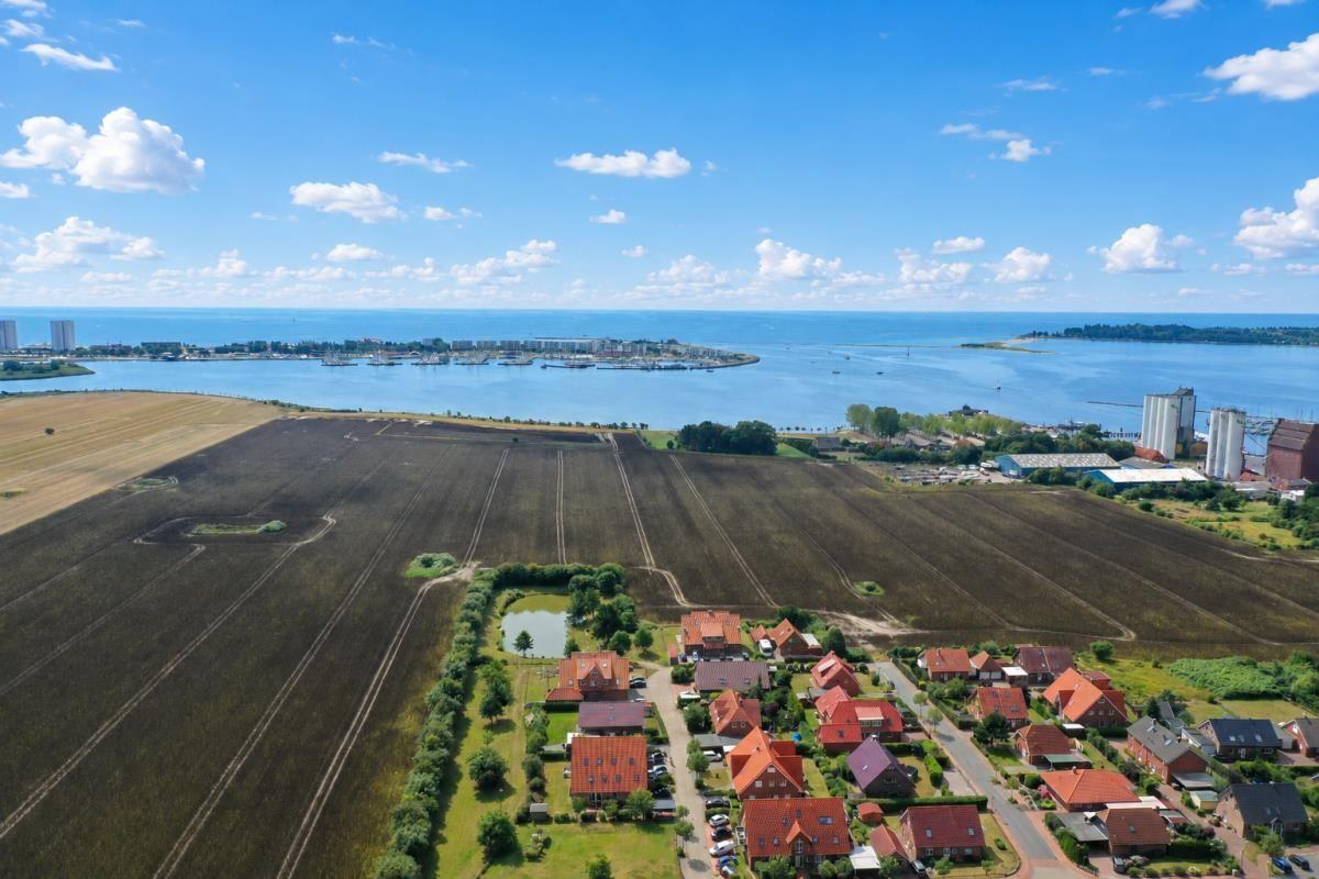 Luftbild von Feldern, Häusern und einem Hafen mit Meer im Hintergrund.