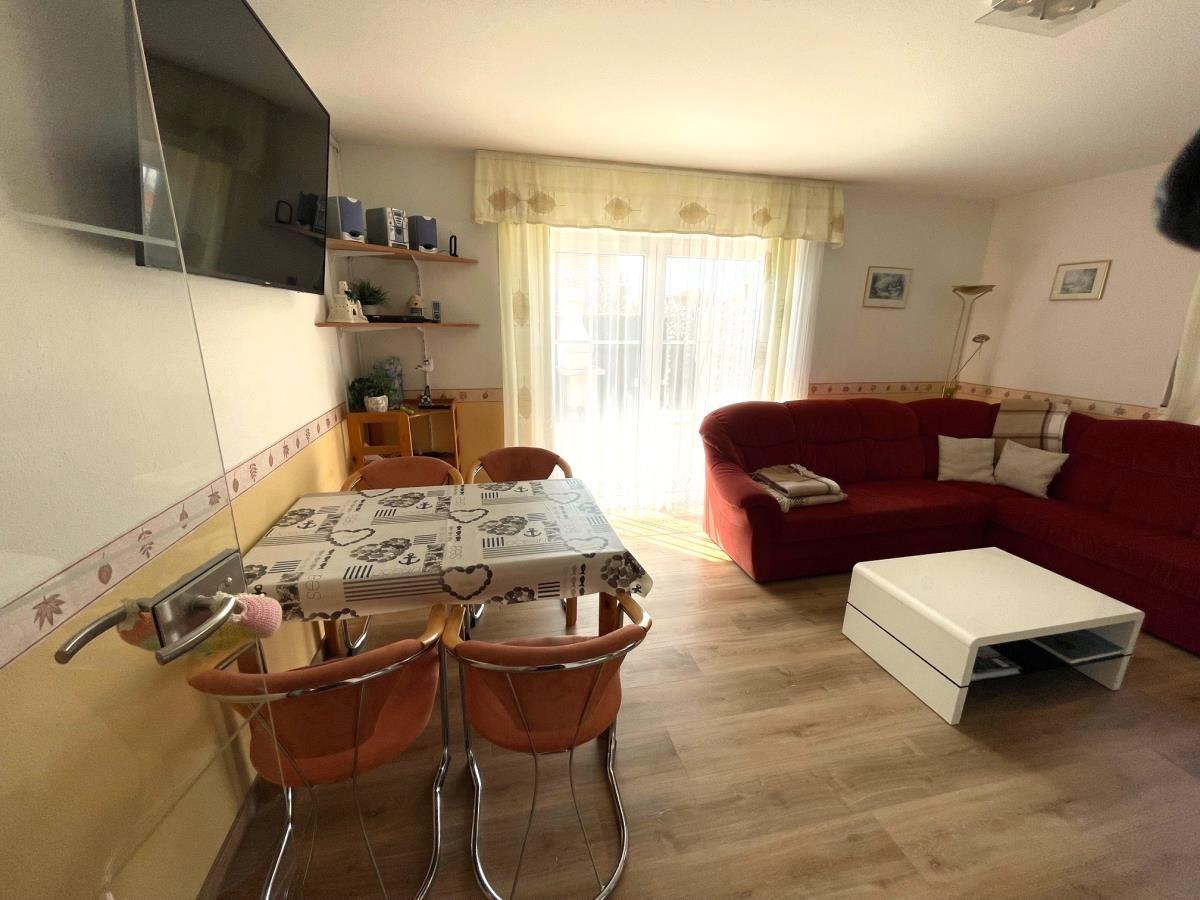 Wohnzimmer mit rotem Sofa, Esstisch und TV an der Wand.