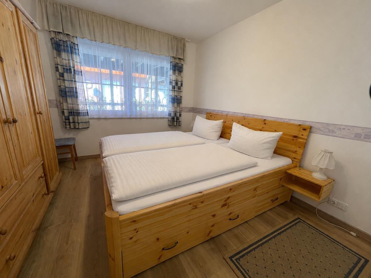 Schlafzimmer mit Holzbett, Kleiderschrank und Fenster mit Vorhängen.