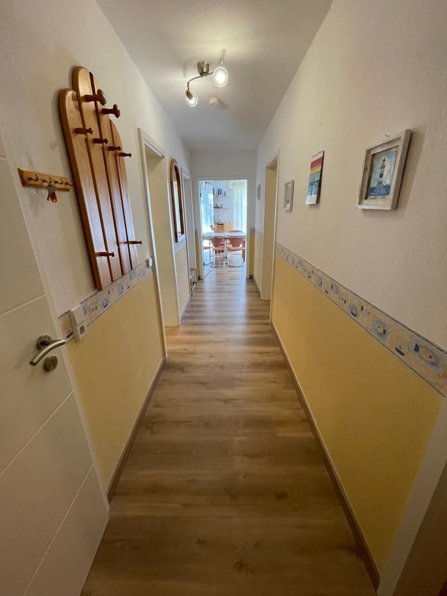 Flur mit Holzboden, gelben Wänden und Bildern an der Wand.
