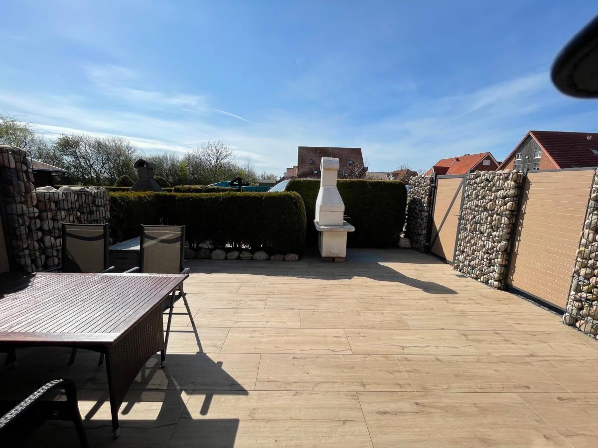 Terrasse mit Tisch, Stühlen und Grill. Umgeben von Hecken und Steinmauern.