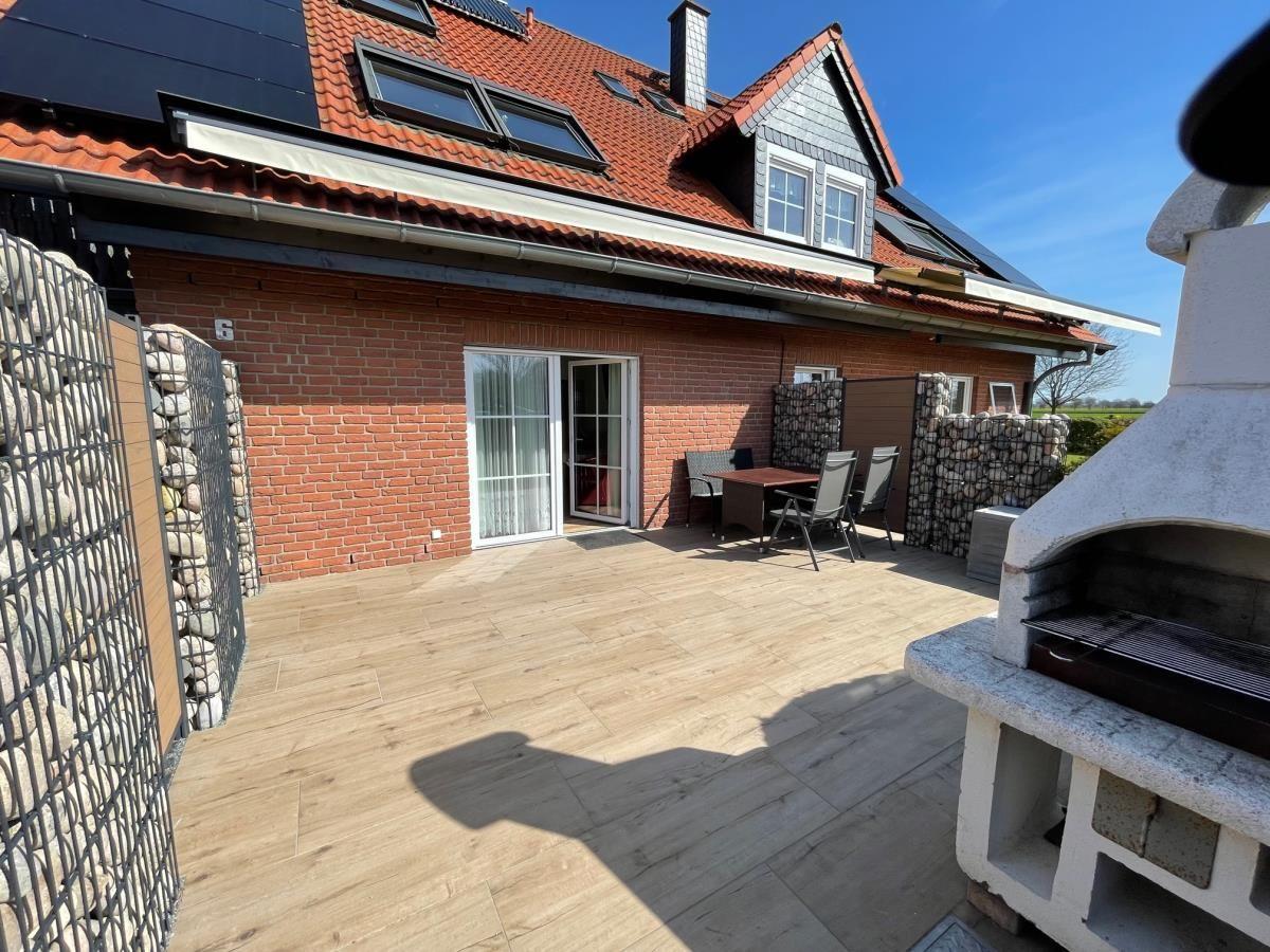Terrasse mit Grill, Tisch und Stühlen vor einem Haus mit rotem Ziegeldach.