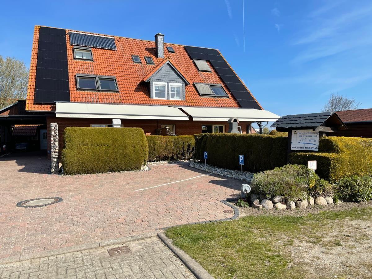 Haus mit Solaranlage, rotem Dach und gepflastertem Hof. Grünhecke und Parkplätze.