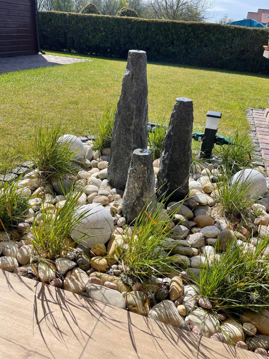 Garten mit Steinarrangement, Kies und Gras. Hintergrund: Rasen und Hecke.
