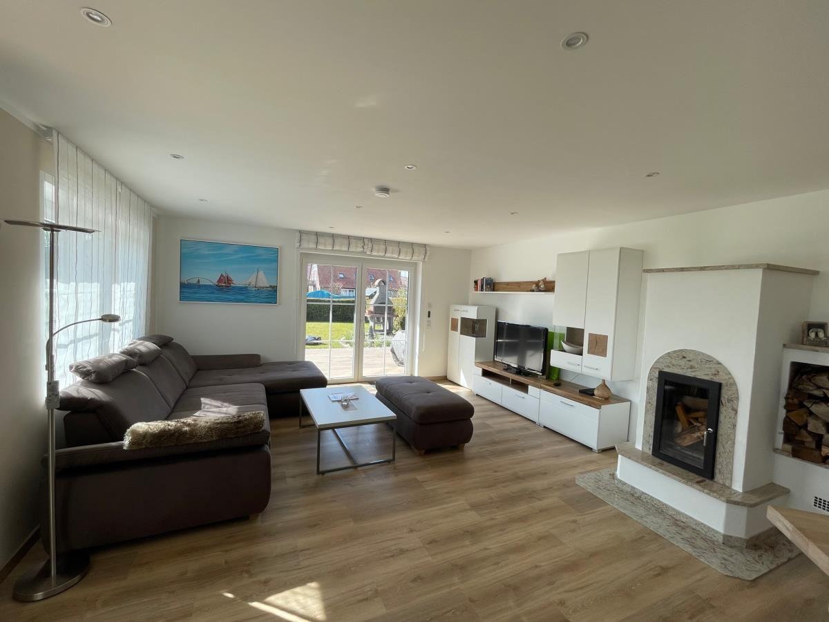 Wohnzimmer mit Sofa, Kamin und TV. Fenster zum Garten. Holzdielenboden.