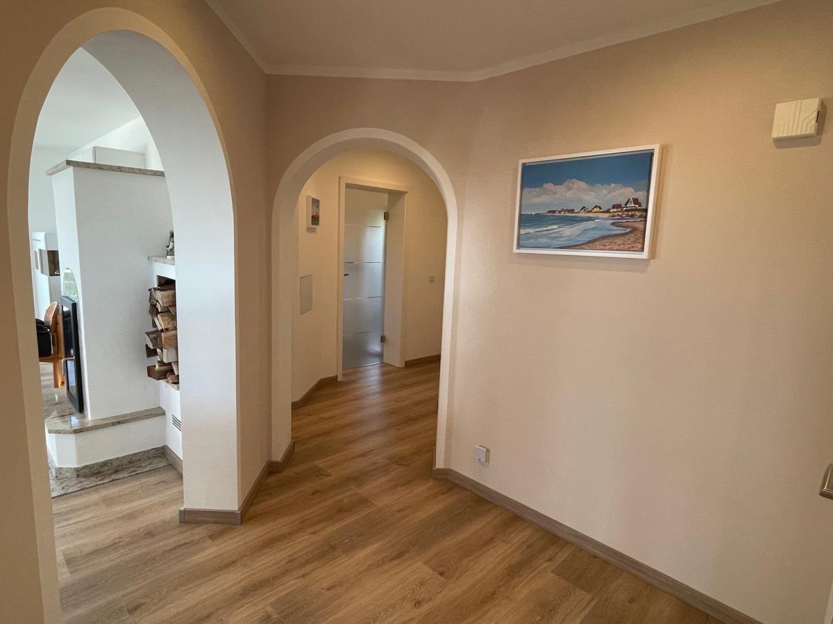 Flur mit Holzboden und Bogenöffnungen. Wandbild zeigt Strand.
