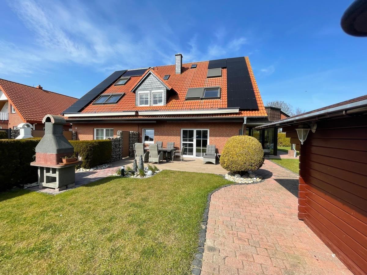 Haus mit Terrasse, Grill und Garten. Dach mit Solarpaneelen und Fenstern.