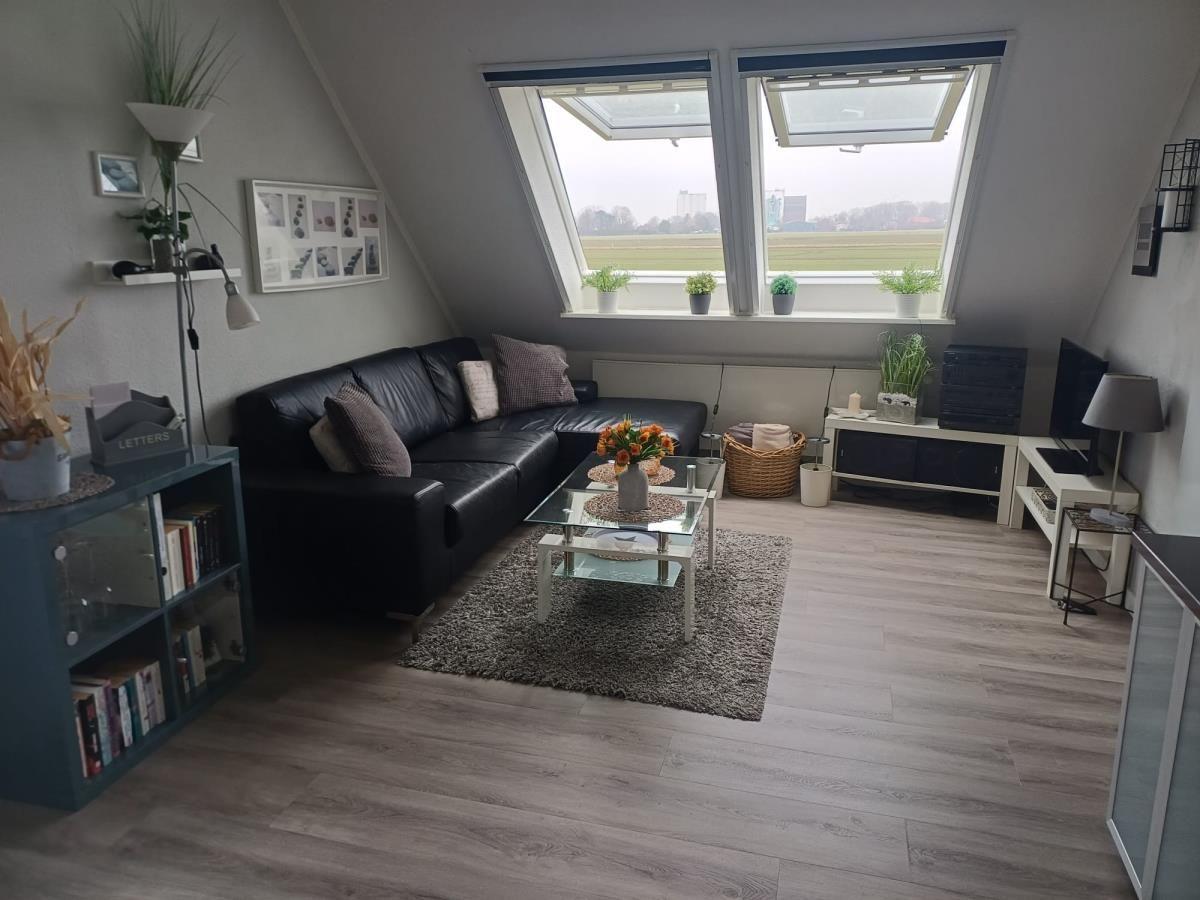 Wohnzimmer mit Sofa, Glas-Tisch und Dachfenstern. Holzboden und Pflanzen sichtbar.