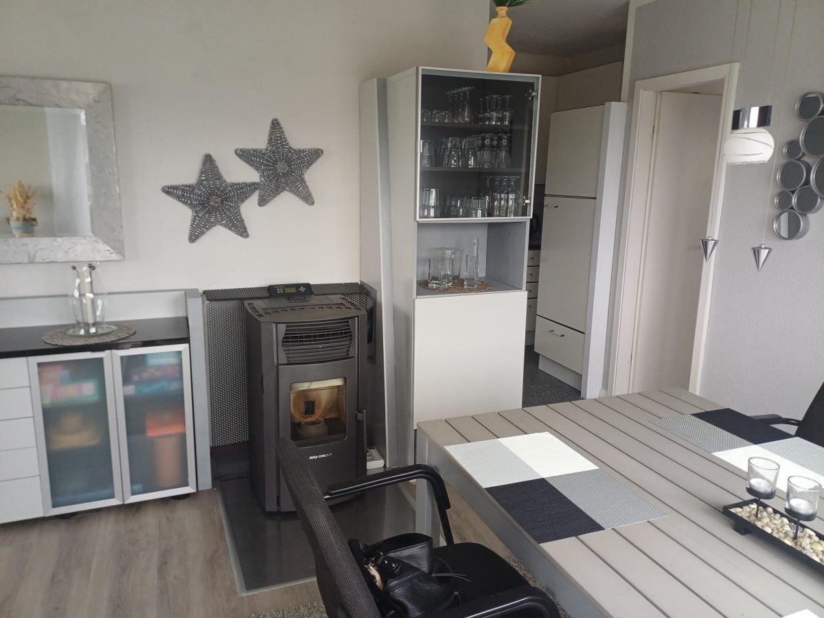 Essbereich mit Tisch, Stühlen und Barhocker. Hintergrund: Küche und Kaminofen.
