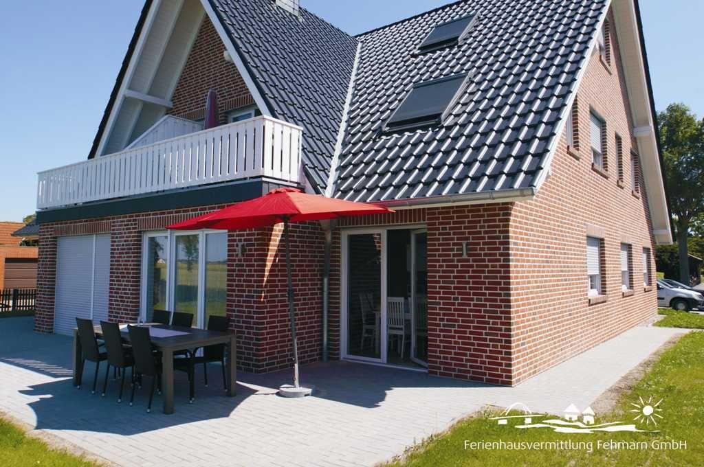 Ferienhaus mit Terrasse, rotem Sonnenschirm und Essbereich. Dachgeschoss mit Balkon.