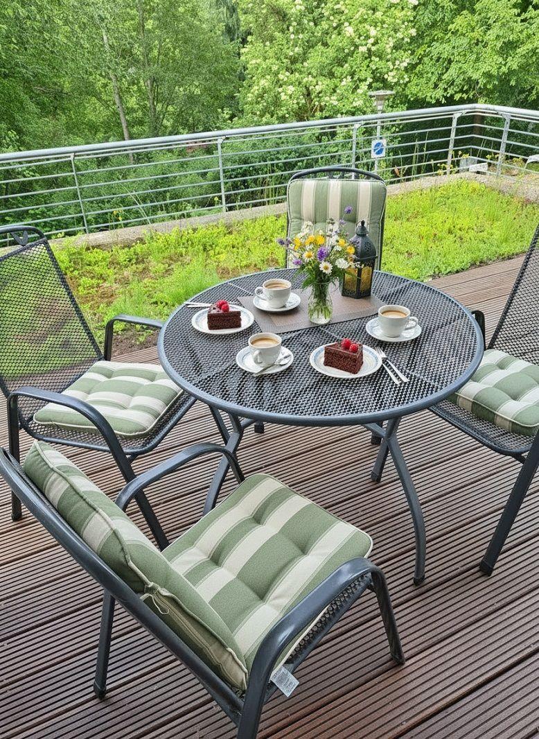 Runder Tisch mit Stühlen auf Terrasse. Auf Tisch stehen Kaffee und Kuchen.