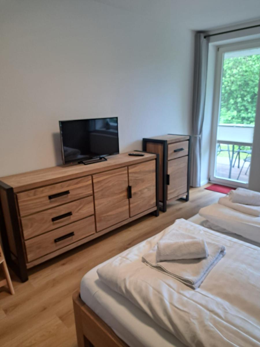Zimmer mit zwei Betten, TV und Balkon. Holzmöbel und helles Holzfußboden.