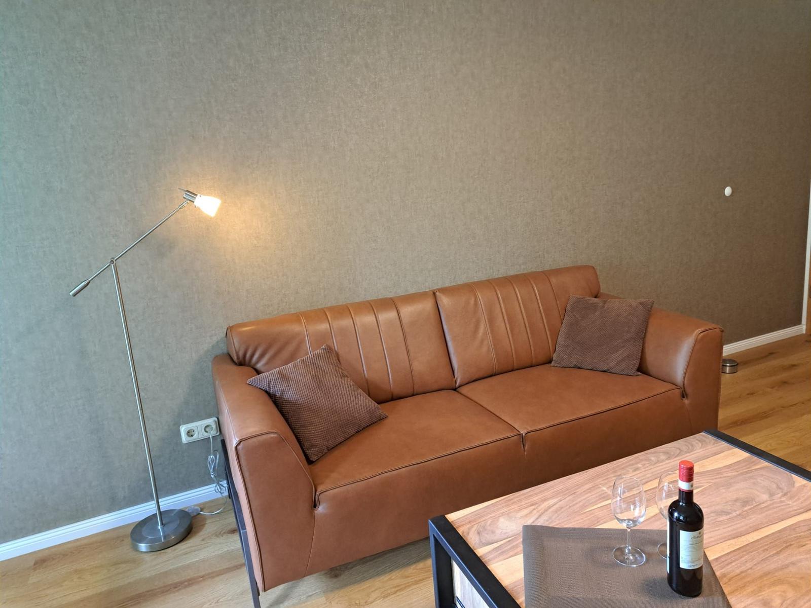 Ein braunes Ledersofa mit Kissen steht vor einer Wand. Auf dem Tisch steht eine Weinflasche und zwei Gläser.