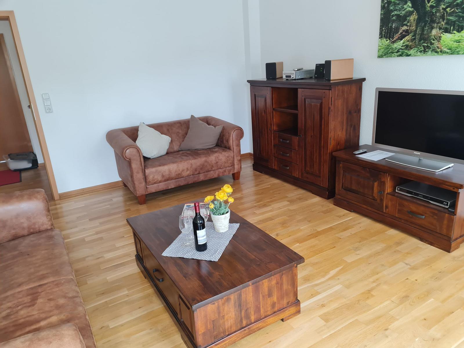 Wohnzimmer mit braunem Sofa, Holztisch und Fernseher.