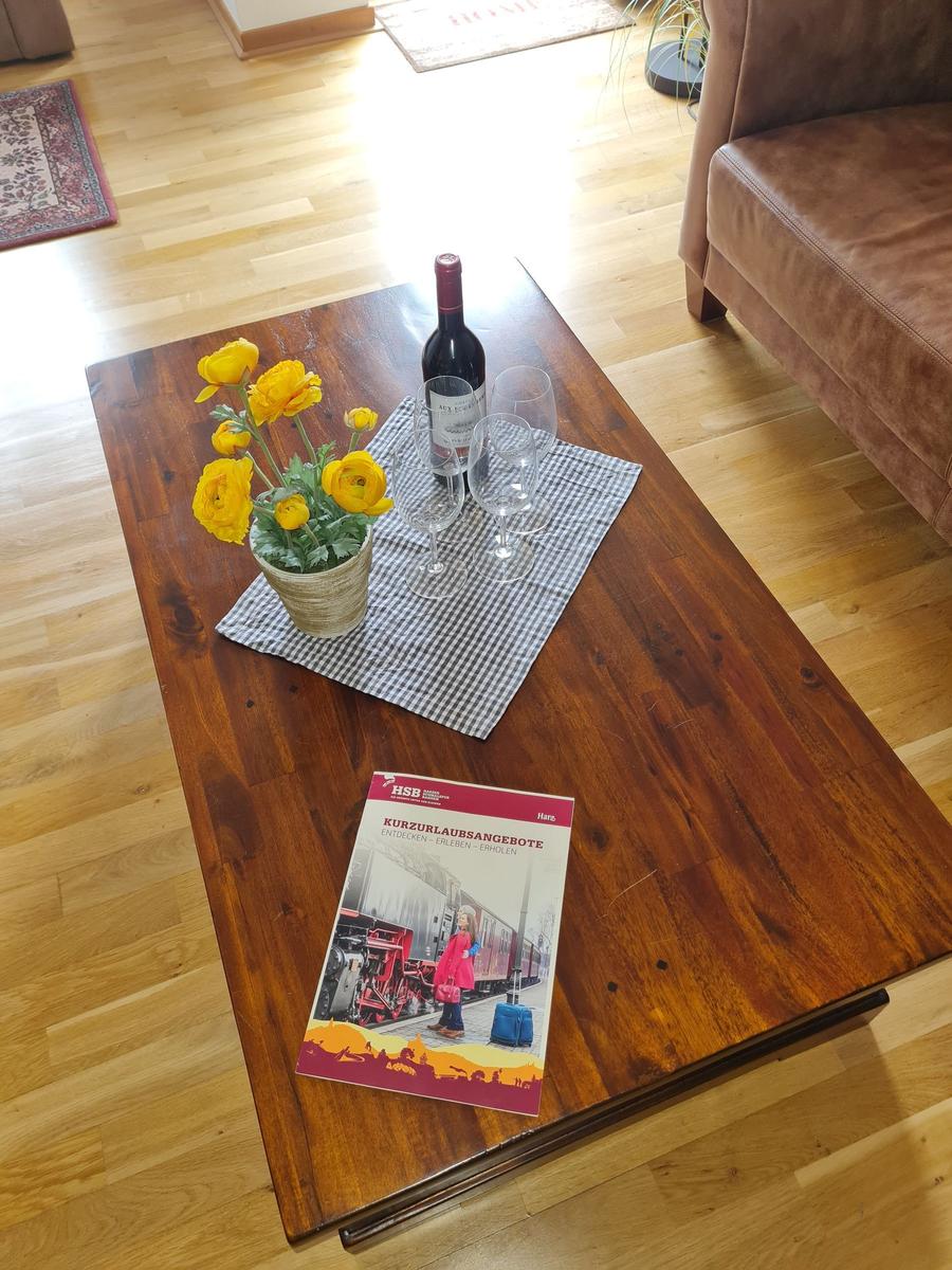 Holztisch mit Blumen, Wein und Reiseflyer im Wohnzimmer.