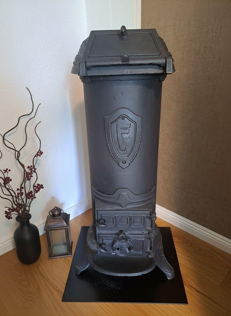 Schwarzer Ofen mit Wappen auf Holzboden neben Vase und Laterne.