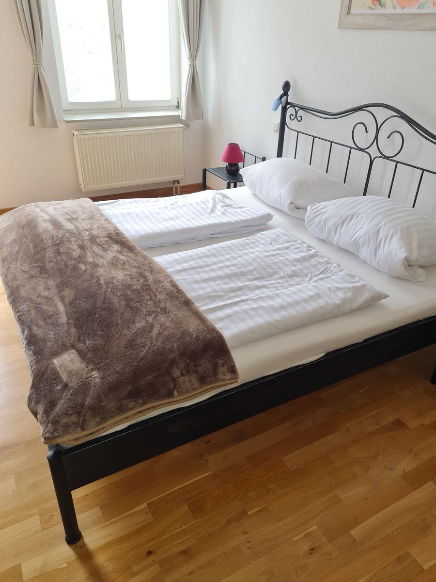 Schlafzimmer mit Doppelbett, Fenster, Heizkörper und Holzboden.