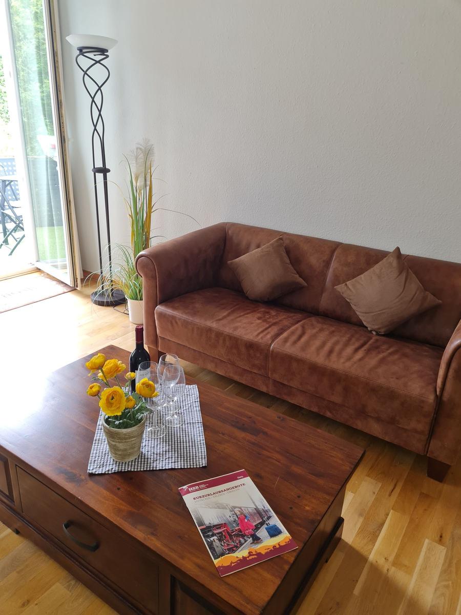 Ein Wohnzimmer mit braunem Sofa, Holztisch und gelben Blumen.