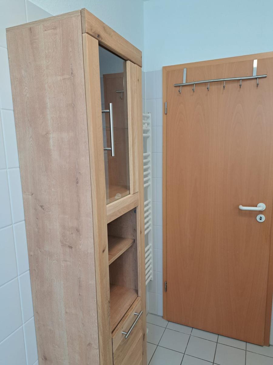 Holzschrank mit Glasfront und Schubladen neben einer Tür mit Haken.
