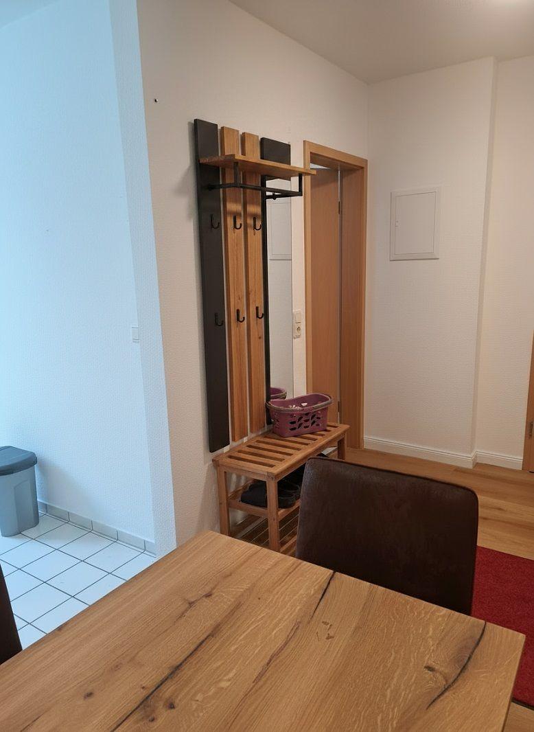 Eingangsbereich mit Holzgarderobe, Sitzbank und Tisch. Hintergrund: Tür und Wand.