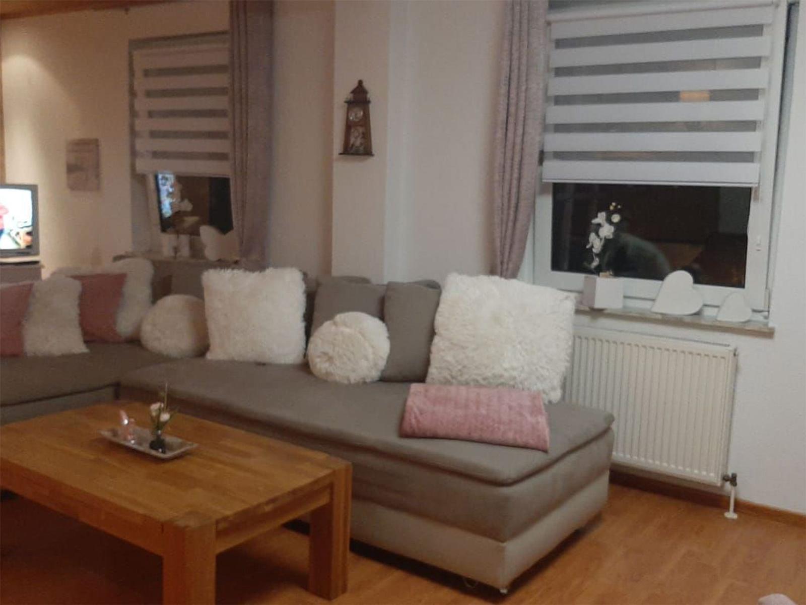 Ein Wohnzimmer mit grauem Sofa, Holztisch und Fenster mit Jalousie.
