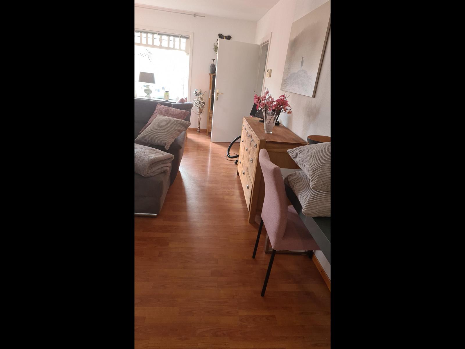 Wohnzimmer mit Sofa, Schreibtisch und Stuhl. Holzboden und Fenster mit Blick.